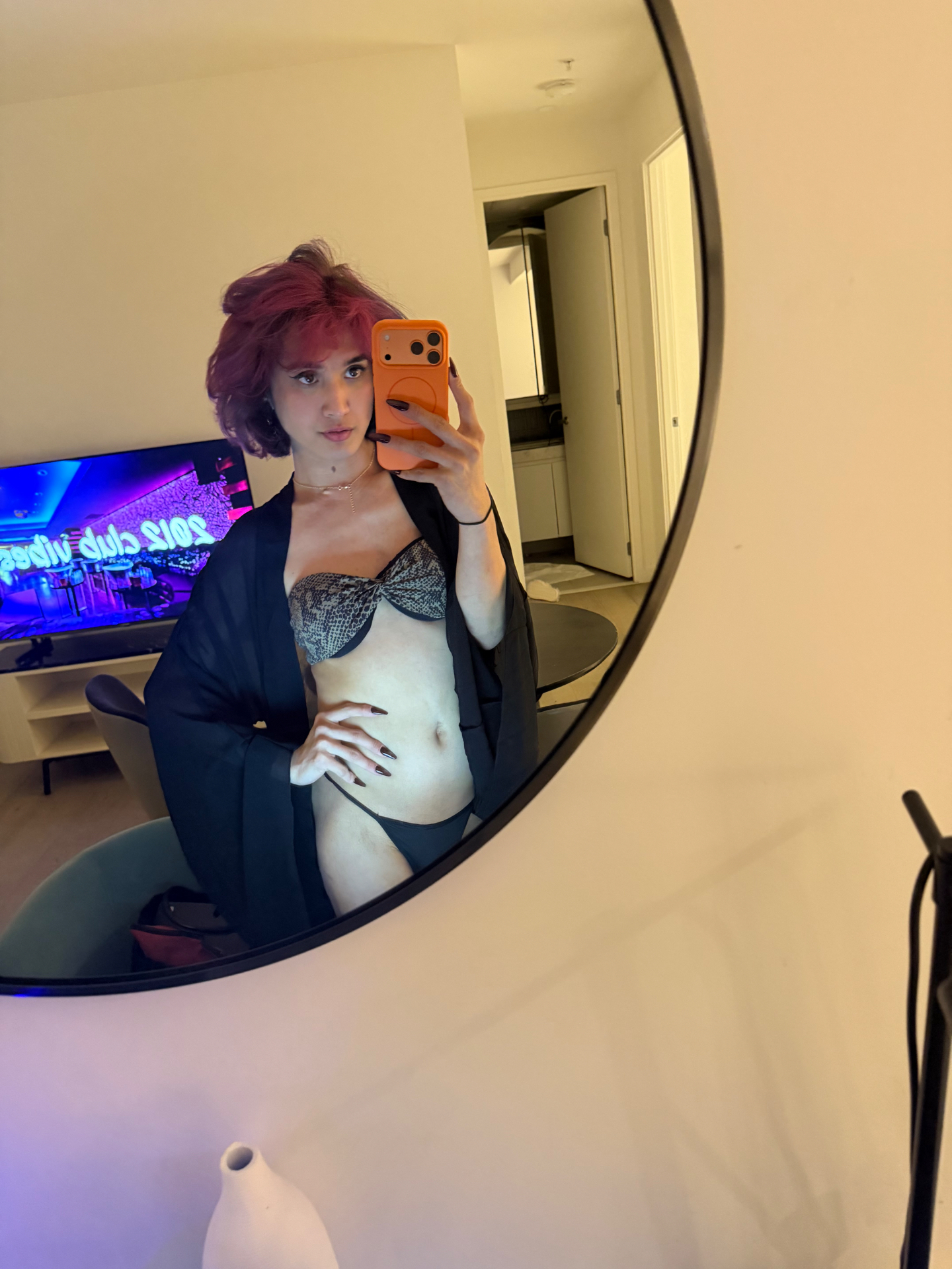 POR$CHA in a sheer black robe reflected in a round wall mirror