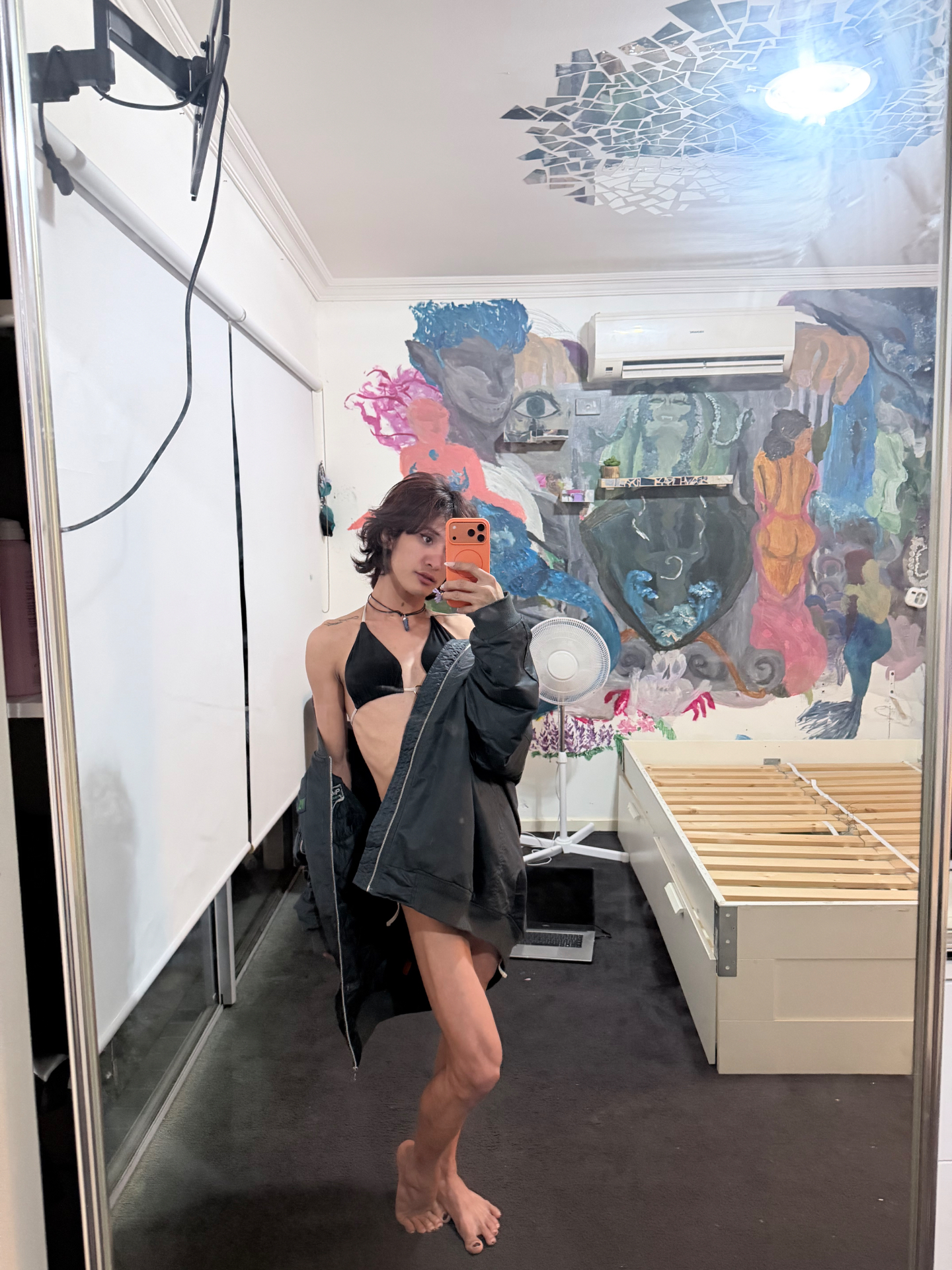 POR$CHA in a black jacket before a painted mural, full-length mirror self-portrait