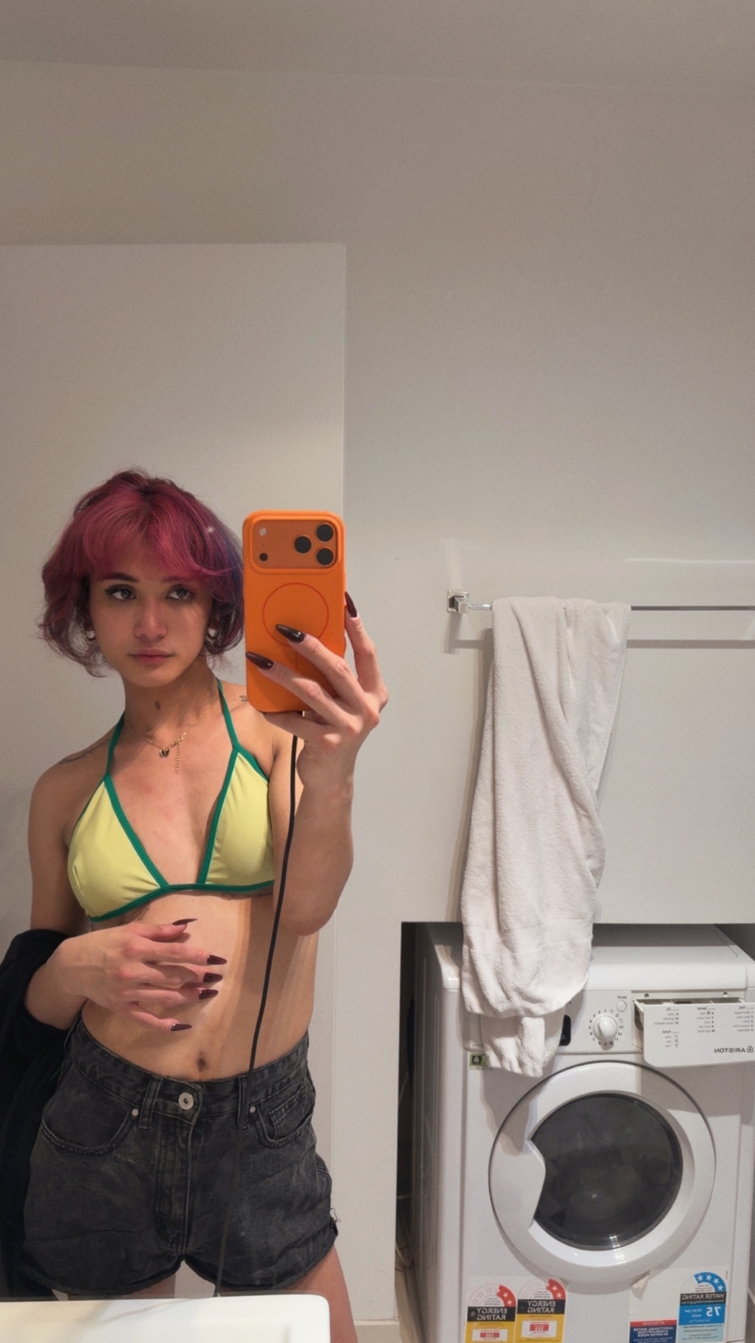 POR$CHA with pink hair in a yellow top and denim shorts, mirror self-portrait