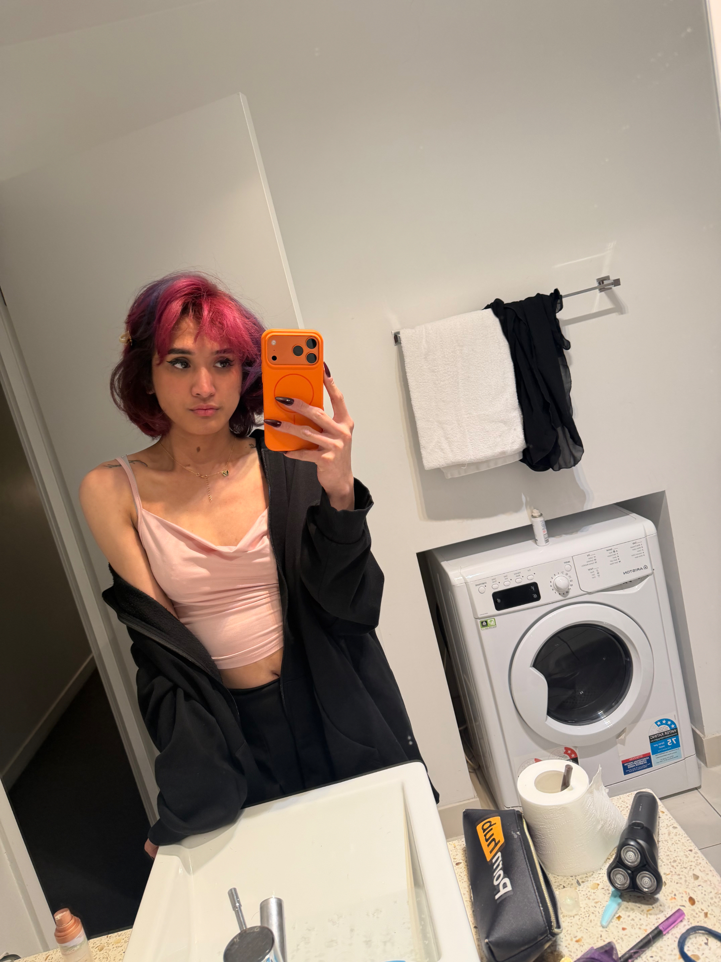POR$CHA in a pink top and black hoodie, bathroom mirror self-portrait