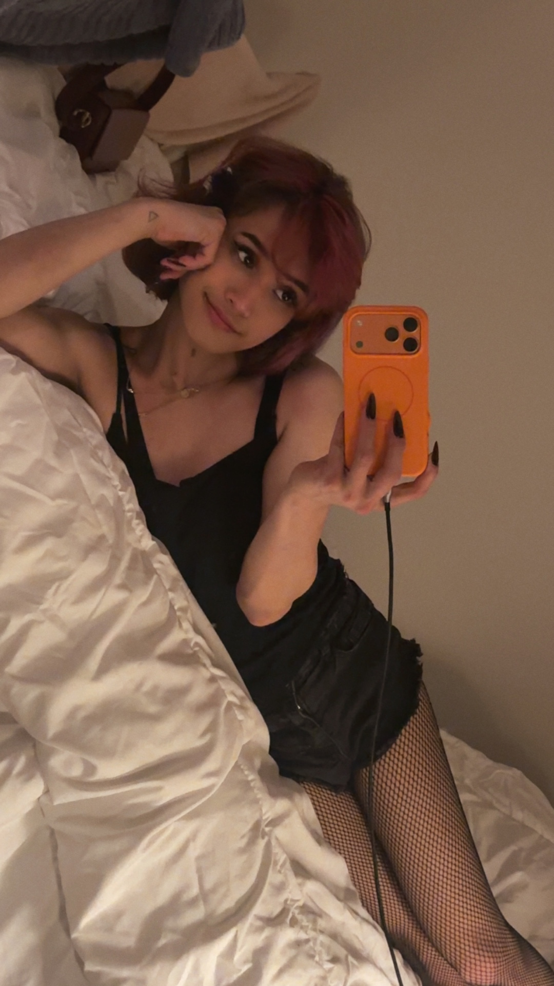 POR$CHA in black dress and fishnets, lying in bed mirror self-portrait