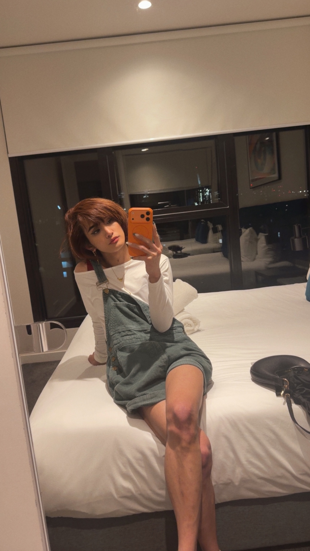 POR$CHA in white top and overalls on a hotel bed, mirror self-portrait