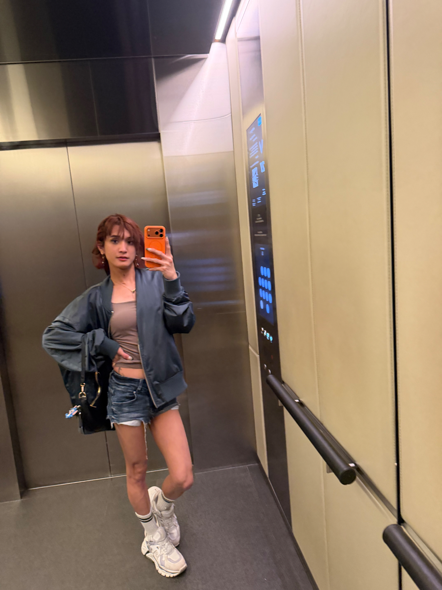 POR$CHA in bomber jacket and shorts, elevator mirror self-portrait