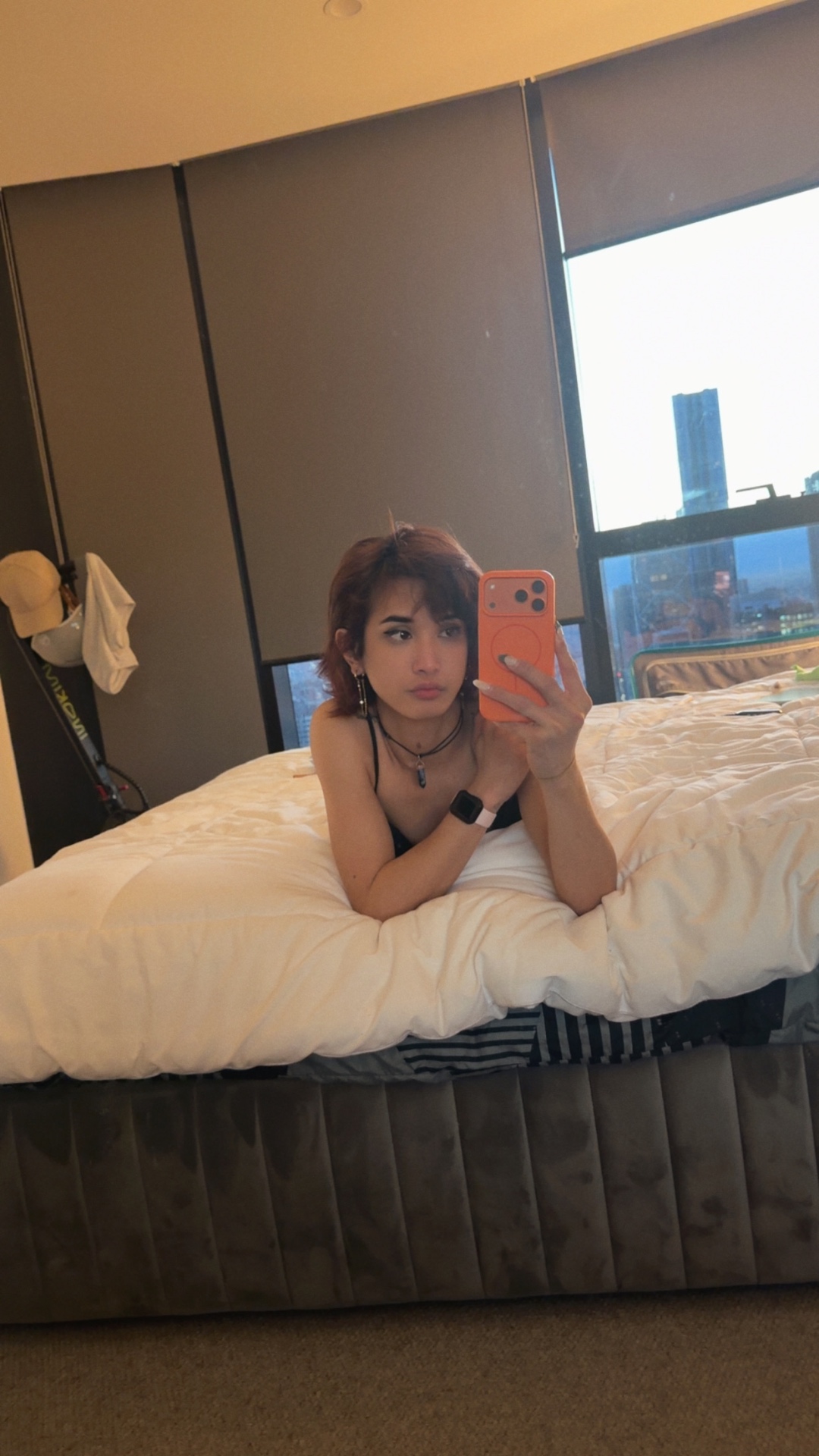 POR$CHA reclining on a bed with a city view, mirror self-portrait