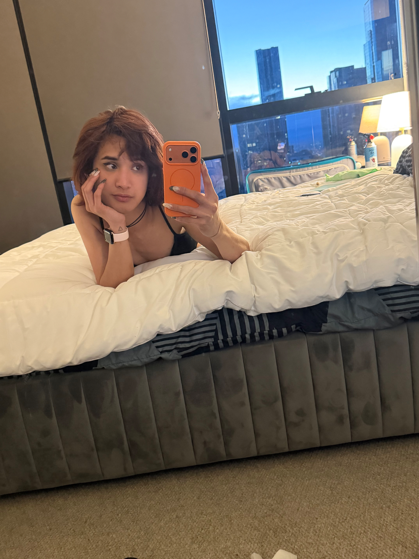 POR$CHA lying on a bed by a city window, mirror self-portrait