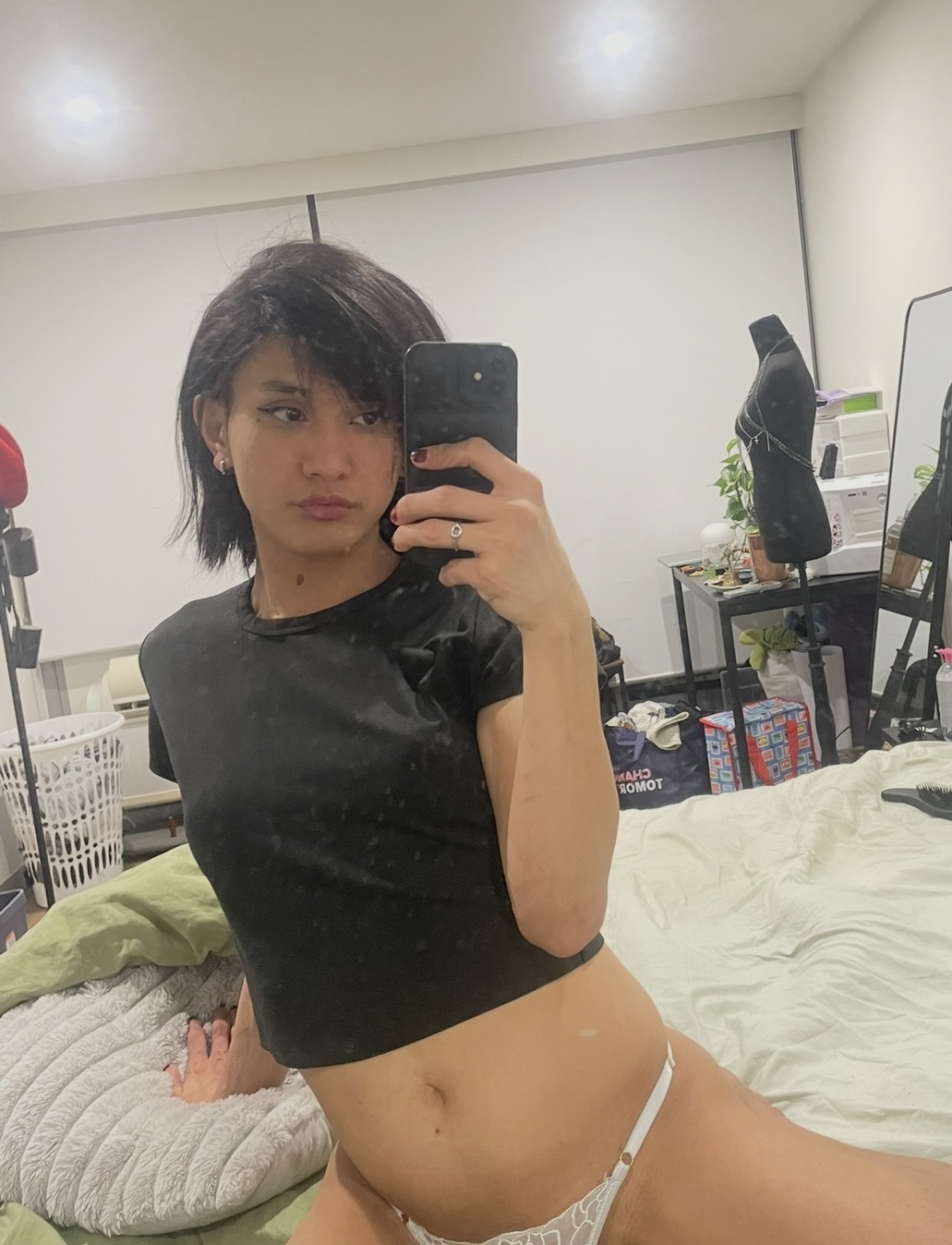 POR$CHA in a black cropped shirt, mirror self-portrait on green bedding
