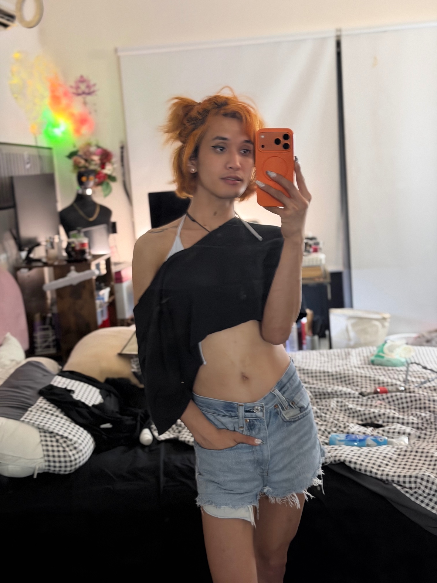 POR$CHA in black top and denim shorts, colorful bedroom mirror self-portrait
